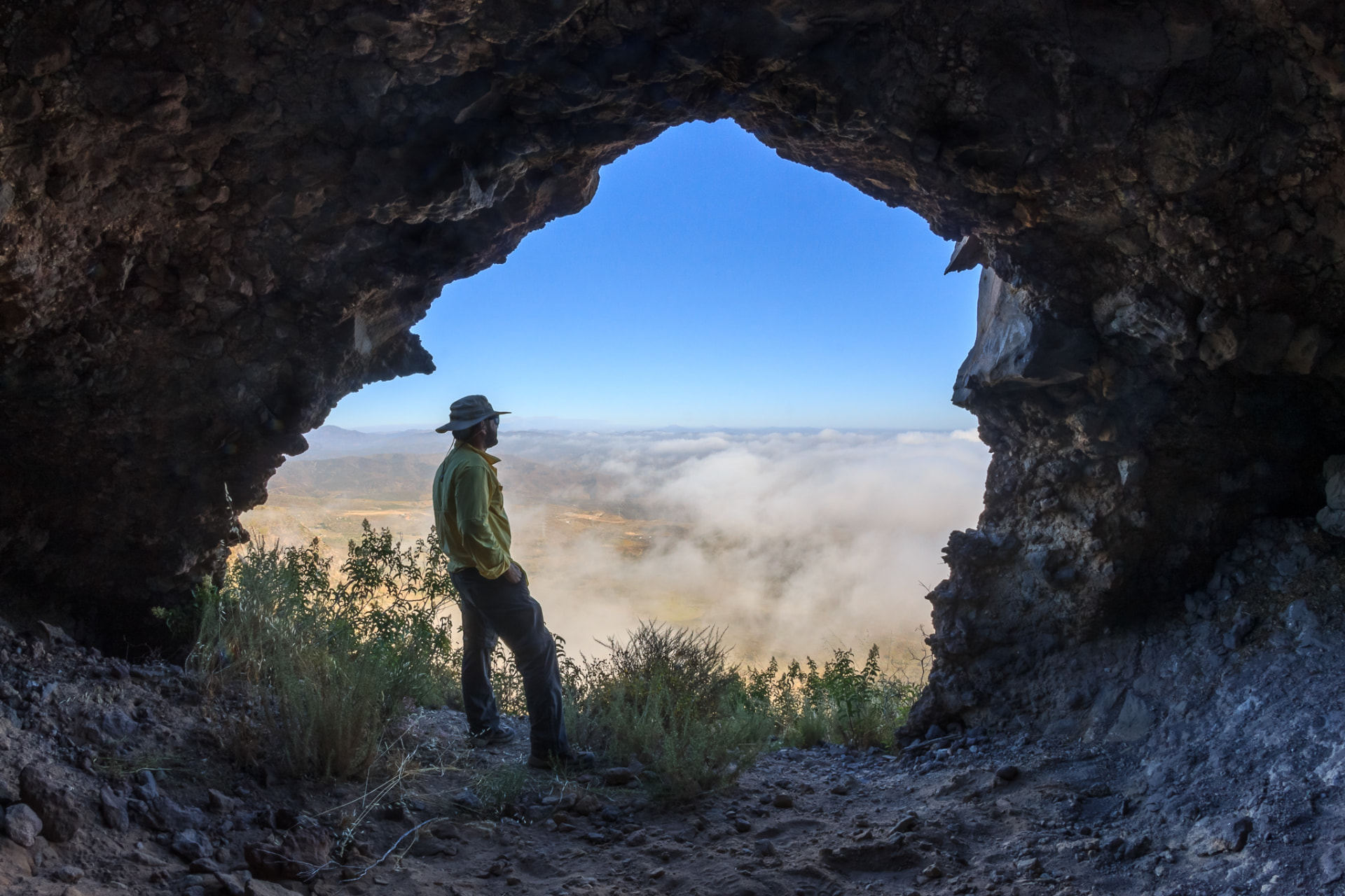 Senderista en la entrada de una cueva del Cerro del Coronel sobre un mar de nubes